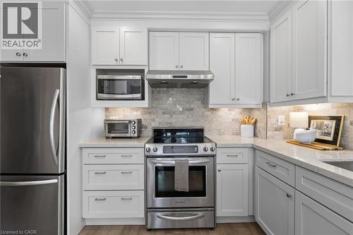 Stainless steel appliances, light-toned cabinetry, light-toned stone countertops, natural stone tile backsplash, and wood-finish flooring - 1610 Heathside Crescent, Pickering, ON 