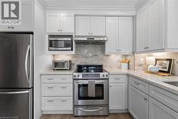 Stainless steel appliances, light-toned cabinetry, light-toned stone countertops, natural stone tile backsplash, and wood-finish flooring - 