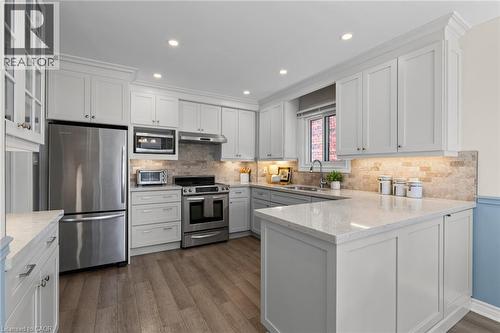 White cabinetry with crown molding, stainless steel appliances, light-toned backsplash, light-toned countertops, and wood-finish flooring - 1610 Heathside Crescent, Pickering, ON 
