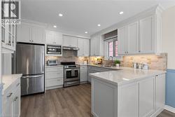 White cabinetry with crown molding, stainless steel appliances, light-toned backsplash, light-toned countertops, and wood-finish flooring - 