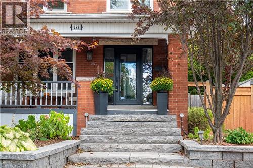 Brick exterior with a prominent front entrance, stone steps, and a landscaped garden with mature trees - 283 Plains Road W, Burlington, ON 