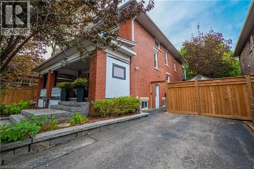 Brick exterior with white trim, covered front porch, stone steps, and a paved driveway with a wood fence - 283 Plains Road W, Burlington, ON 