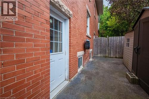 Red brick exterior with a white paneled door, offering access to a paved side yard - 283 Plains Road W, Burlington, ON 