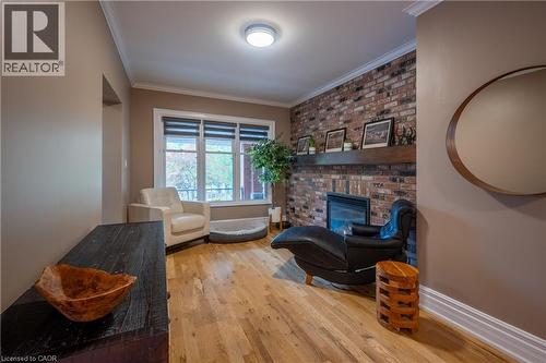 Hardwood flooring throughout, a brick accent wall with an integrated fireplace, and a wood mantel shelf - 283 Plains Road W, Burlington, ON 