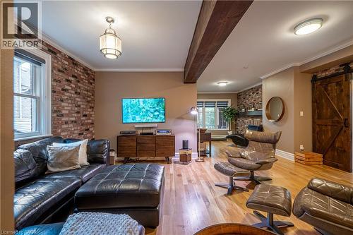 Hardwood flooring throughout, exposed brick accent wall, wood-finish ceiling beams, recessed lighting, and a barn door entry - 283 Plains Road W, Burlington, ON 