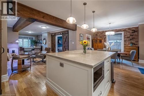 Kitchen island with stone countertop, natural wood-finish flooring, wood beam accents, brick wall, and pendant lighting - 283 Plains Road W, Burlington, ON 