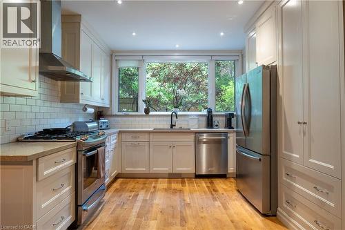 Kitchen featuring a window overlooking greenery, wood-finish flooring, white shaker cabinetry, stainless steel appliances, and subway tile backsplash - 283 Plains Road W, Burlington, ON 