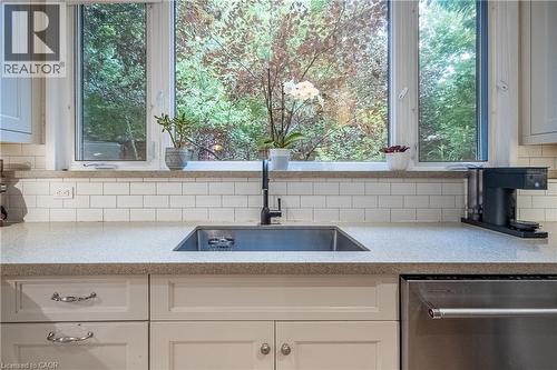 Under-mount sink with a matte black faucet, light-toned countertop, subway tile backsplash, white shaker-style cabinetry, and stainless steel dishwasher - 283 Plains Road W, Burlington, ON 