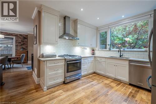 Kitchen featuring wood-finish flooring, white cabinetry, stainless steel appliances, subway tile backsplash, and a large window - 283 Plains Road W, Burlington, ON 