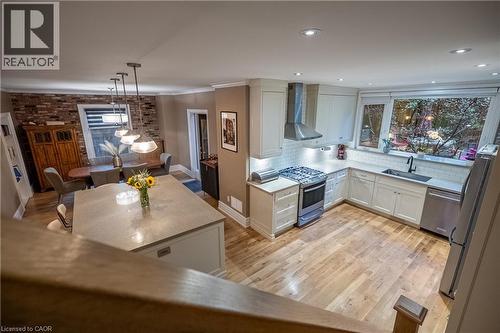 Open-concept kitchen and dining area featuring light wood-finish flooring, a kitchen island with a light-toned countertop, white cabinetry, and stainless steel appliances - 283 Plains Road W, Burlington, ON 