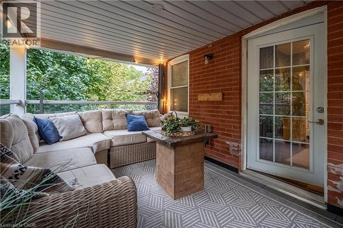 Covered patio with a brick exterior, white French-pane door, and glass panel railing - 283 Plains Road W, Burlington, ON 