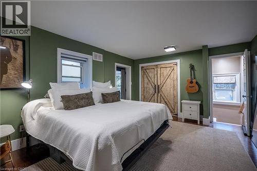 Rich olive-toned walls, wood-finish flooring, two windows with white trim, a barn door style closet, and white overhead lighting - 283 Plains Road W, Burlington, ON 