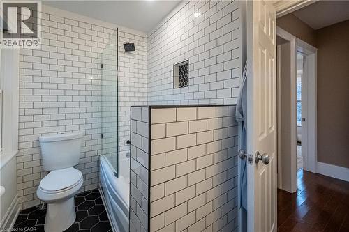 Bathroom featuring subway tile walls, black hexagonal floor tiles, a built-in shower niche, and a glass shower partition - 283 Plains Road W, Burlington, ON 