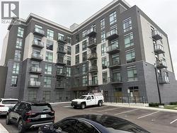 Modern multi-story building featuring a facade of grey brick and light-colored panels, private balconies with glass railings, and a dedicated surface parking area - 