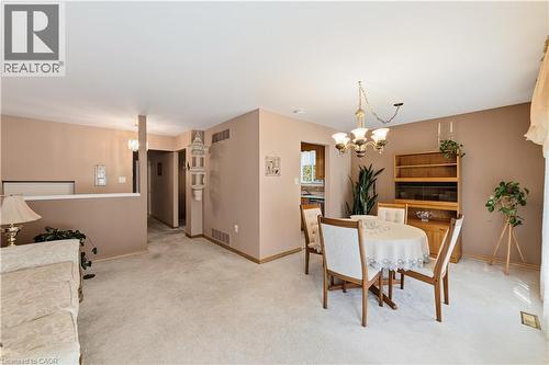Open-concept living and dining area featuring neutral carpeting, a brass-finish chandelier, and a half-wall partition - 450 Brigadoon Drive, Hamilton, ON 