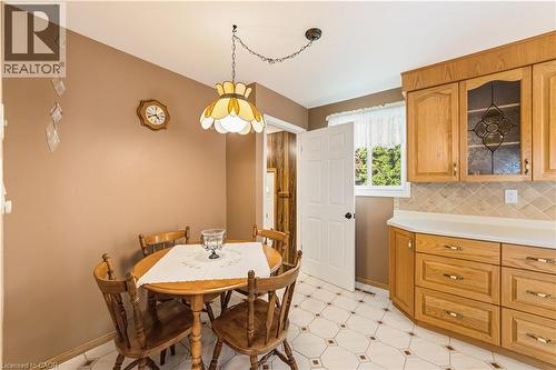 Dining area featuring a decorative ceiling light fixture, patterned floor ceramic tiles, light wood cabinetry with glass-front accents, and a window with natural light - 450 Brigadoon Drive, Hamilton, ON 