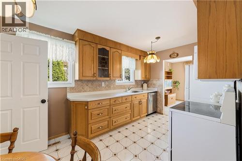 Kitchen featuring wood cabinetry, light countertops, stainless steel dishwasher, white over the range microwave, fridge and stove, geometric pattern flooring, and a tiled backsplash - 450 Brigadoon Drive, Hamilton, ON 
