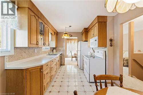Galley kitchen featuring wood cabinetry, light countertops, a tiled backsplash, and patterned tile flooring - 450 Brigadoon Drive, Hamilton, ON 