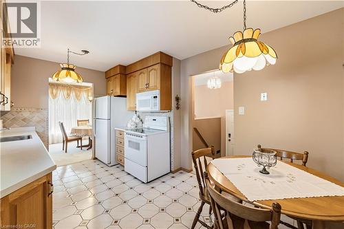 Kitchen featuring wood cabinetry, white appliances, patterned tile flooring, and light countertops - 450 Brigadoon Drive, Hamilton, ON 