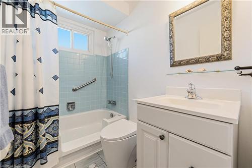 Bathroom featuring a white vanity with integrated sink, an ornate framed mirror, a glass display shelf, light blue square wall tiling (original still in great shape), and a white bathtub modified for - 450 Brigadoon Drive, Hamilton, ON 