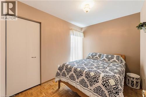 Neutral-toned bedroom featuring wood-finish parquet flooring, a window with sheer white curtains, and a flush-mount ceiling light - 450 Brigadoon Drive, Hamilton, ON 