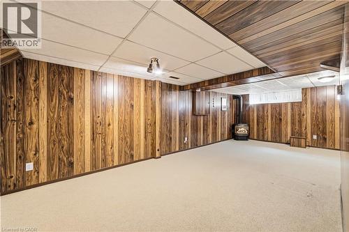 Spacious recreation room featuring gas fireplace, wood-finish paneling, a drop ceiling, window and light-toned carpeting - 450 Brigadoon Drive, Hamilton, ON 
