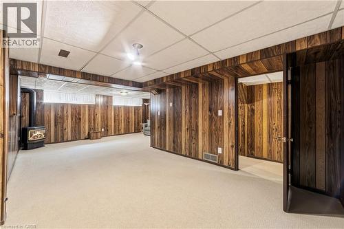 Spacious recreation room featuring gas fireplace, wood paneling, light-colored carpeting, and a drop ceiling - 450 Brigadoon Drive, Hamilton, ON 