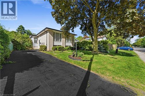 Front exterior featuring light-colored brick siding, newly sealed asphalt driveway, mature trees, and established - 450 Brigadoon Drive, Hamilton, ON 