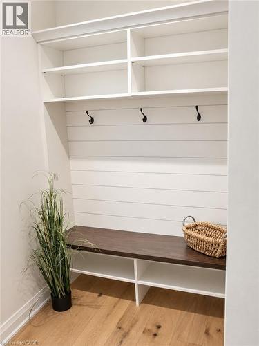 Built-in storage bench with dark wood-finish top, white shiplap-style backing, three matte black hooks, and upper open shelving - 515 Hamilton Drive, Ancaster, ON 