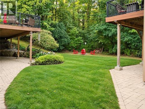 Expansive backyard featuring a manicured lawn, two elevated wood decks with black railings, and a stone paver patio - 515 Hamilton Drive, Ancaster, ON 