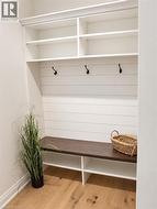 Built-in storage bench with dark wood-finish top, white shiplap-style backing, three matte black hooks, and upper open shelving - 