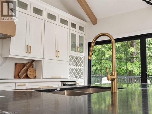 Contemporary kitchen featuring white shaker cabinetry with brass hardware, a black waterfall-edge island countertop, and a brass gooseneck faucet with pull-down spray - 515 Hamilton Drive, Ancaster, ON 