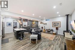 Spacious room featuring wood-finish flooring, recessed lighting, and a dark-toned kitchen island with a light-colored countertop - 