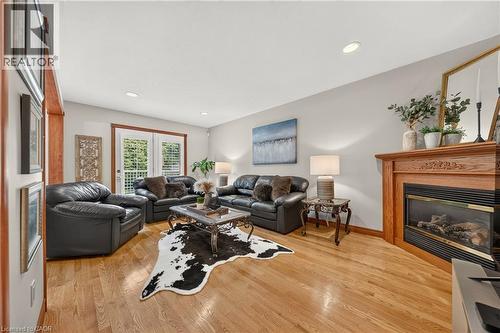 Hardwood flooring, corner fireplace with wood mantel, recessed lighting, and white French doors - 52 Archwood Crescent, Cambridge, ON 