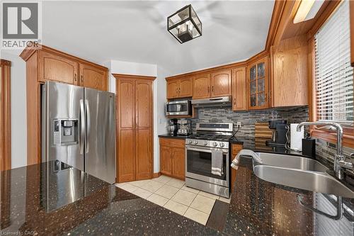 Stainless steel appliances, wood cabinetry, dark speckled countertops, tile flooring, and a tiled backsplash - 52 Archwood Crescent, Cambridge, ON 