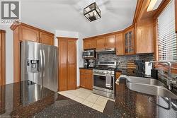 Stainless steel appliances, wood cabinetry, dark speckled countertops, tile flooring, and a tiled backsplash - 
