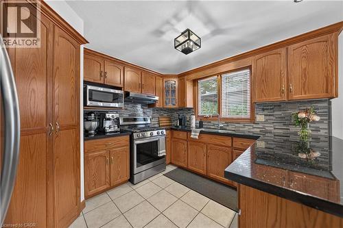 Kitchen with wood cabinetry, black countertops, stainless steel appliances, a mosaic tile backsplash, and a ceiling-mounted light fixture - 52 Archwood Crescent, Cambridge, ON 