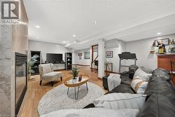 Recessed lighting illuminates this room, featuring light wood-finish flooring and a built-in fireplace with a stone-finish surround - 