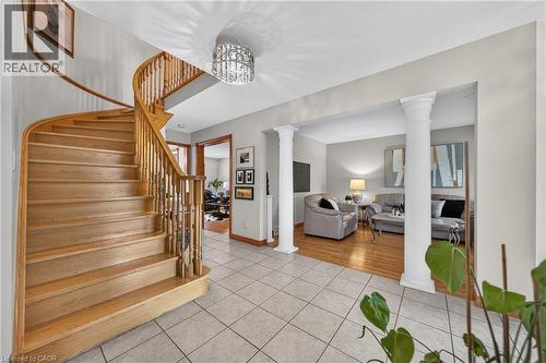 Curved wood staircase with traditional balusters, tile flooring, decorative chandelier, and architectural columns - 52 Archwood Crescent, Cambridge, ON 