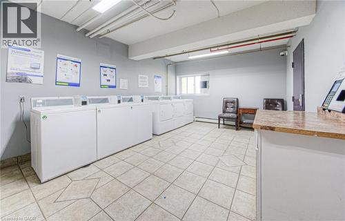 Community laundry room featuring light tile patterned floors, separate washer and dryer, and baseboard heating - 283 Fairway Road N Unit# 501, Kitchener, ON 