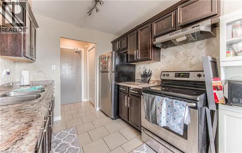 Kitchen with backsplash, appliances with stainless steel finishes, under cabinet range hood, and dark brown cabinetry - 283 Fairway Road N Unit# 501, Kitchener, ON 
