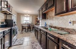 Kitchen featuring stainless steel range with electric stovetop, dark brown cabinets, a chandelier, and a textured ceiling - 