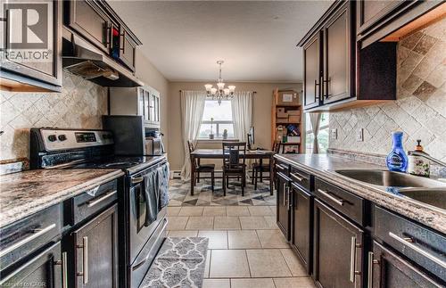 Kitchen with backsplash, electric stove, a chandelier, and dark brown cabinetry - 283 Fairway Road N Unit# 501, Kitchener, ON 
