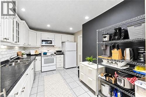 White upper and lower cabinetry, dark countertops, a subway tile backsplash, and a double-basin stainless steel sink - 1270 Gainsborough Drive Unit# 61, Oakville, ON 