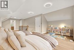 Sloped ceilings with recessed lighting, wood-finish flooring, white paneled door, and a wooden handrail with metal spindles - 