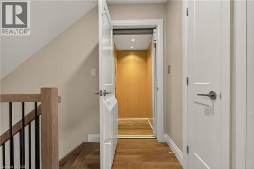 Hardwood flooring, wood-finish stair railing with black spindles, light-colored walls, white trim, and a built-in elevator - 279 Hess Street S, Hamilton, ON 