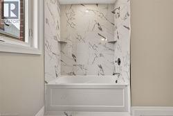 Bathtub with surround of marble-look tile, integrated shelving, and a dark-finish shower head and faucet - 
