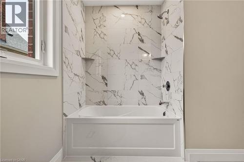 Bathtub with surround of marble-look tile, integrated shelving, and a dark-finish shower head and faucet - 279 Hess Street S, Hamilton, ON 
