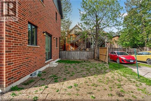 Red brick exterior, black-framed windows, sliding glass door, exterior lighting fixtures, and a side yard with a wooden fence - 279 Hess Street S, Hamilton, ON 
