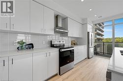 Kitchen with appliances with stainless steel finishes, wall chimney exhaust hood, light wood-type flooring, light stone counters, and white cabinetry - 